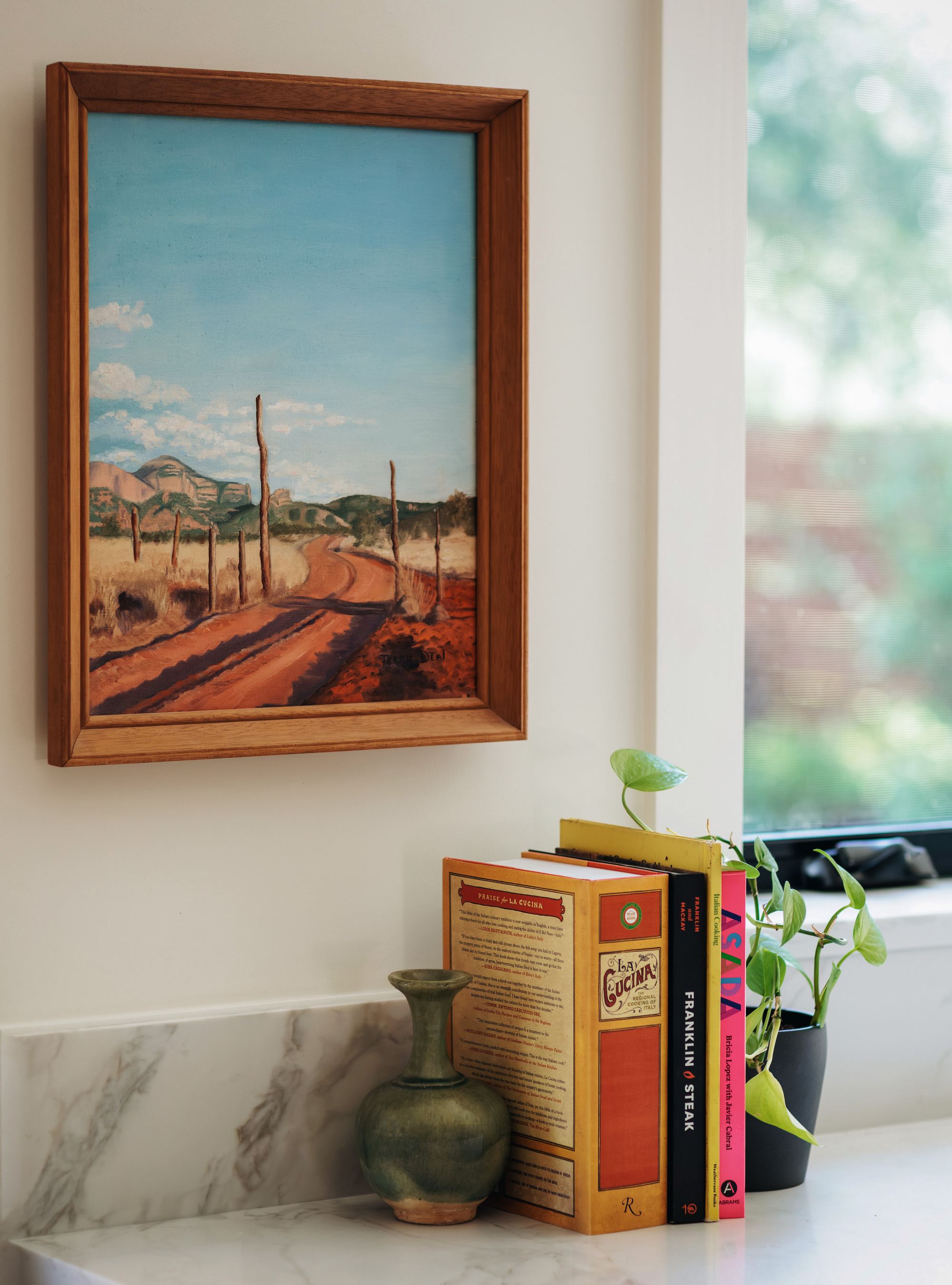 Framed landscape painting above a kitchen counter styled with cookbooks