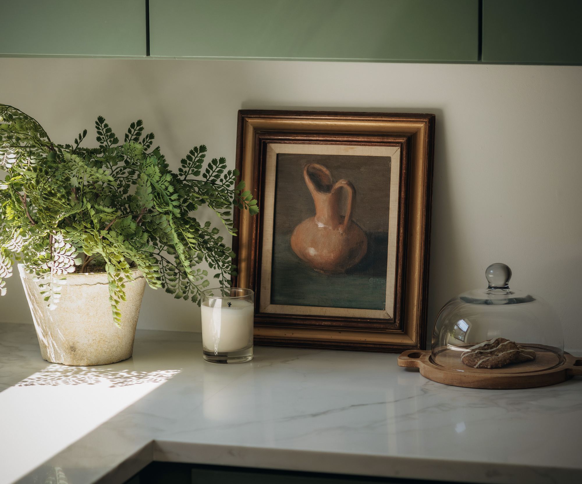 Kitchen counter vignette with a framed still life and a glass cloche