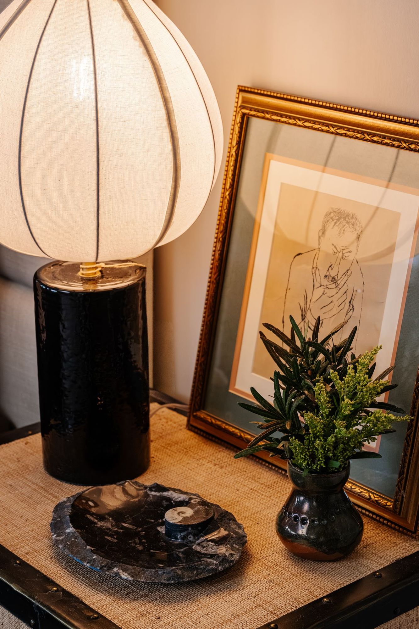 Bedside table styled with a ceramic lamp and framed portrait sketch